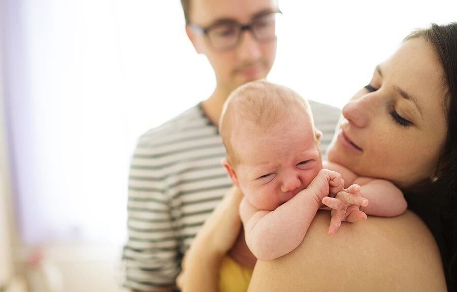 New Mom Holding Crying Baby with Partner in Background
