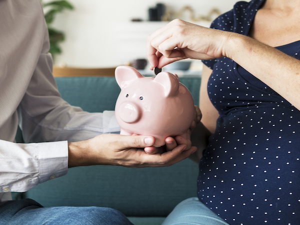 Pregnant couple saving money in piggy bank for pre-baby bucket list