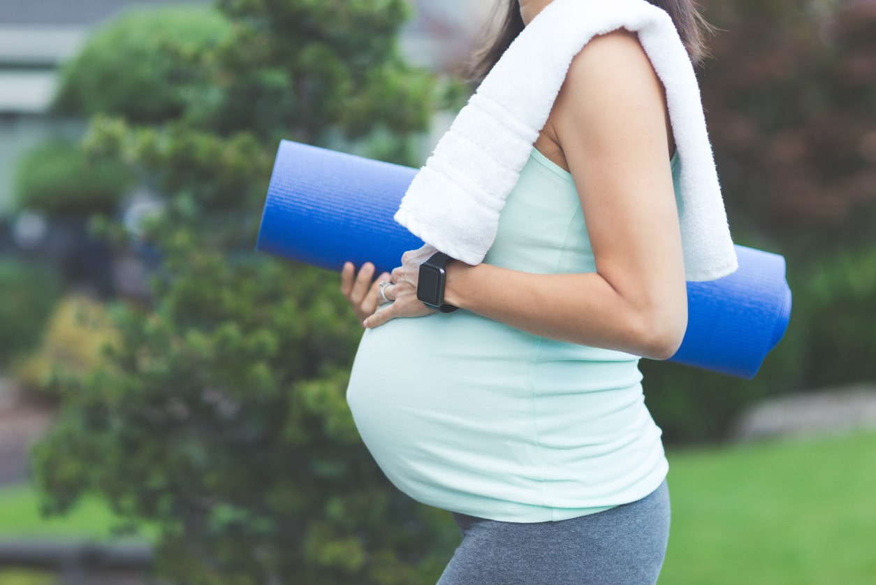Pregnant woman carries yoga mat on her way to the gym.