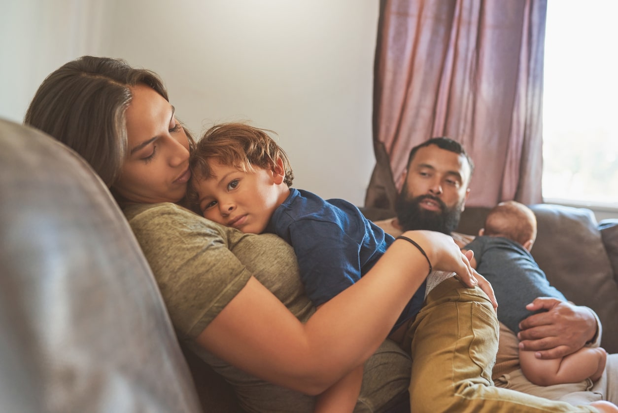 Shot of a little boy resting on his motherâs chest with his baby brother and father in the background stock photo